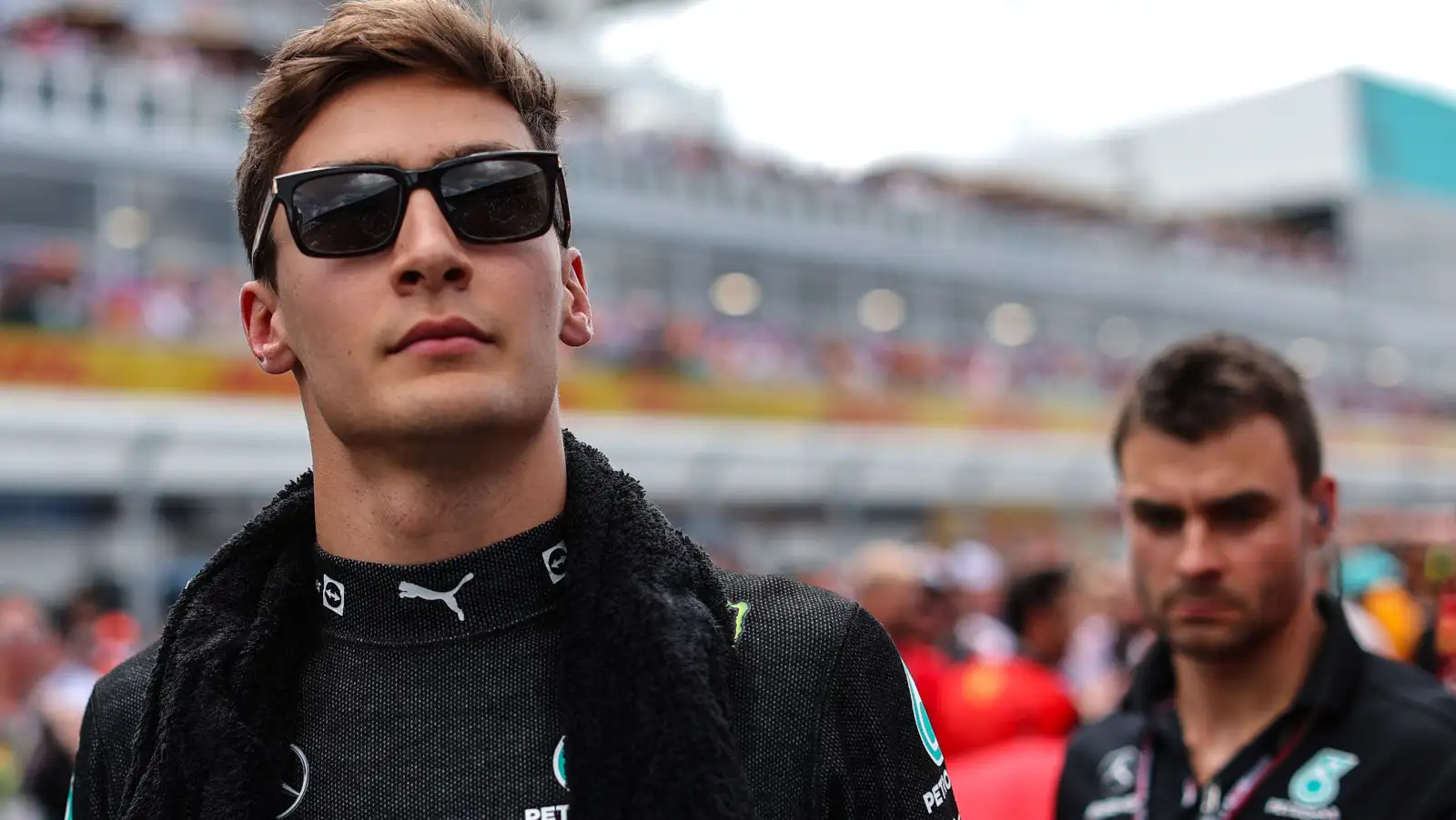 George Russell wearing sunglasses on the grid, Mercedes man behind him. Miami May 2022