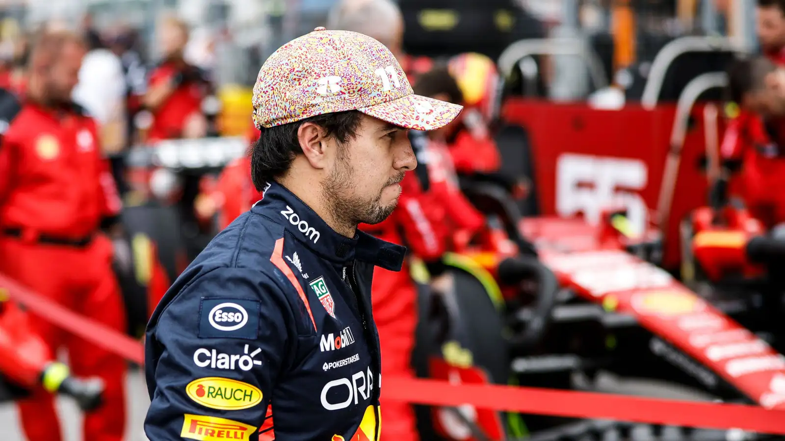 Unhappy Sergio Perez walks past a Ferrari.