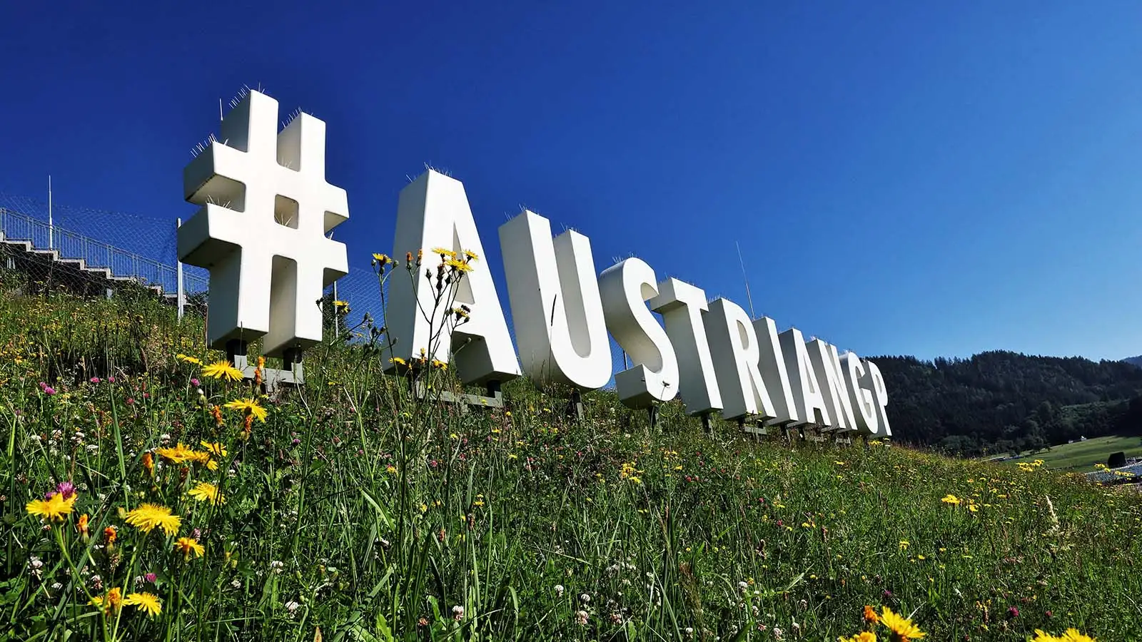 A huge display is nestled on the lush green hills of the Red Bull Ring with a sign that reads #AustrianGP