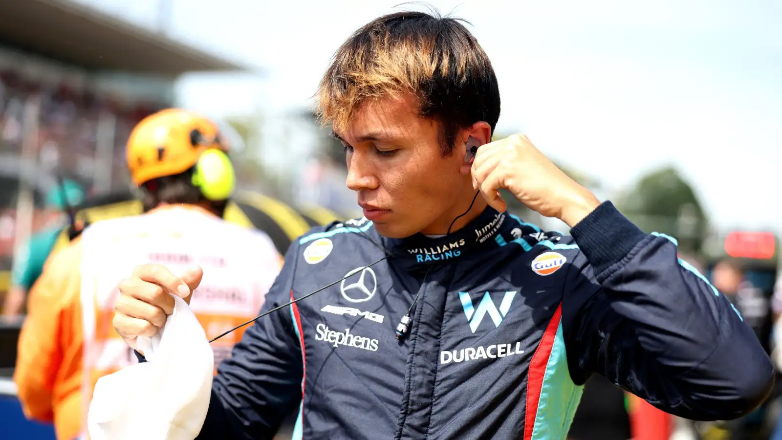 Williams driver Alex Albon putting in his ear piece while standing on the grid.