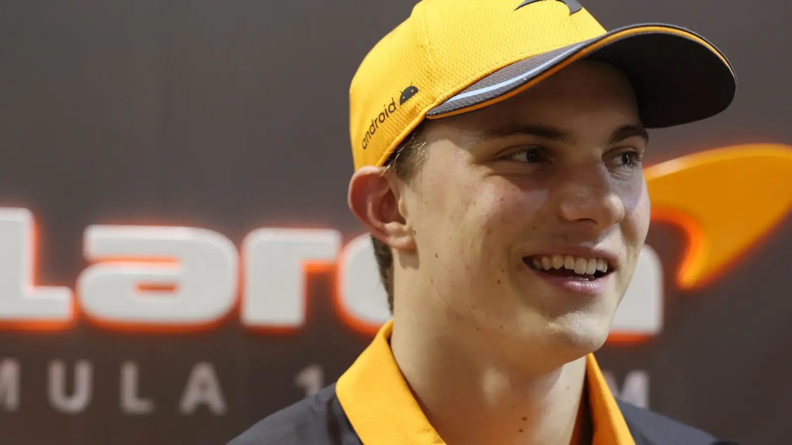 Oscar Piastri smiling while standing in front of the McLaren logo.