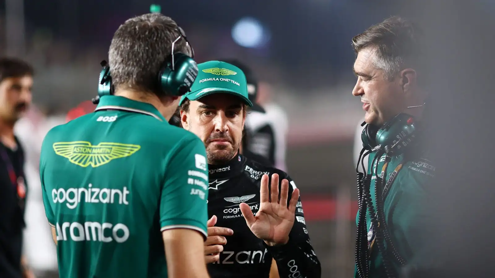 Fernando Alonso with his hand raised as he speaks with team members on the grid in Qatar.