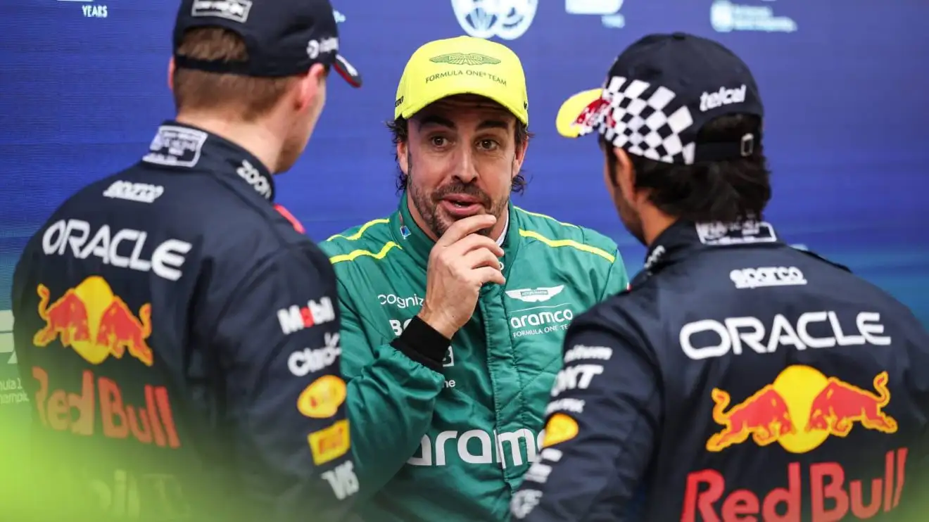 Max Verstappen and Sergio Perez stand with their backs turned, talking to Fernando Alonso in parc ferme