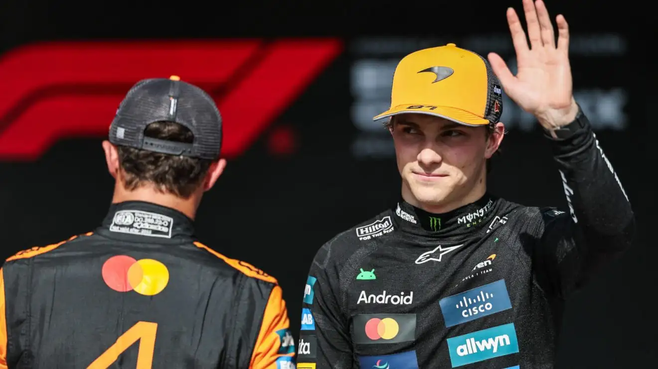 Oscar Piastri waves in front of Lando Norris