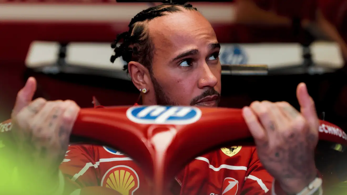 Lewis Hamilton glances to the side as he holds on to the halo while lowering himself into the cockpit of his Ferrari SF-25