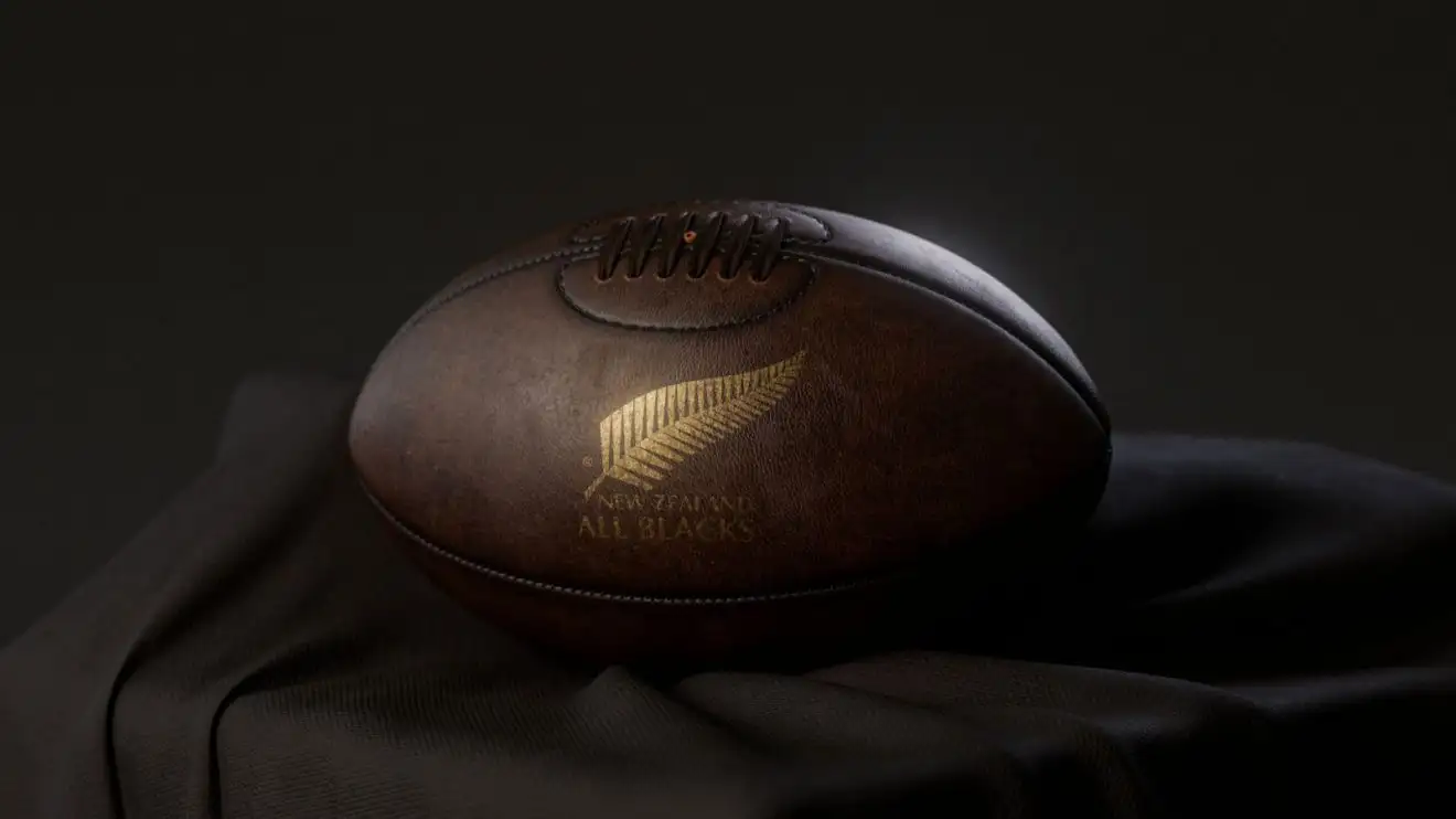 A 3D render of a vintage leather rugby ball with a gold New Zealand Rugby logo resting on a draped cloth.