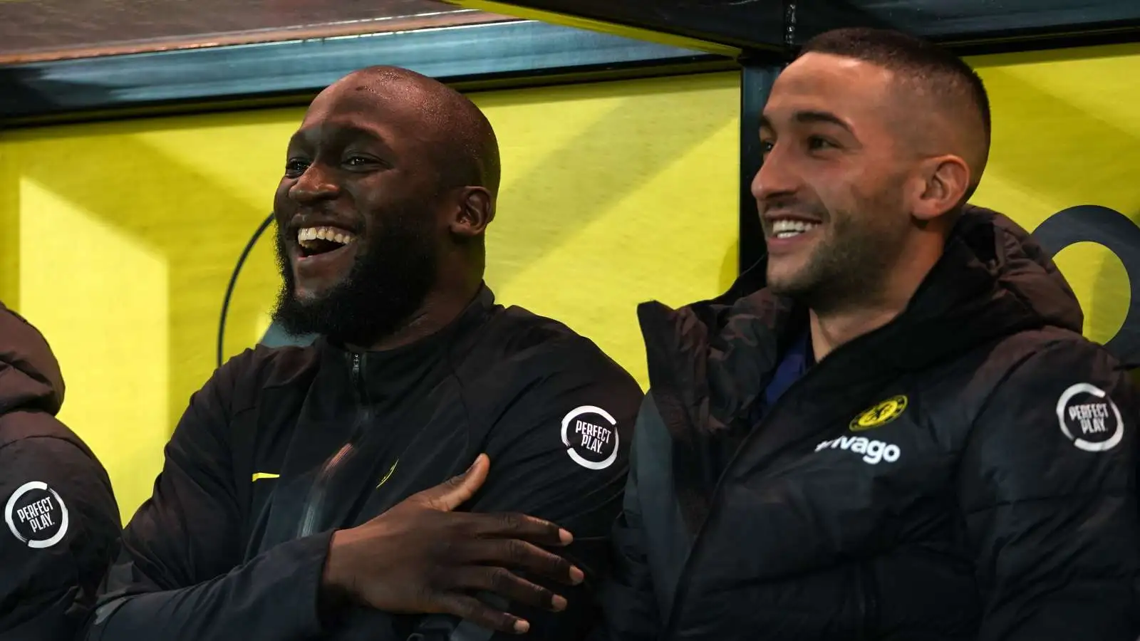 Romelu Lukaku and Hakim Ziyech smiling while sitting on the bench for Chelsea